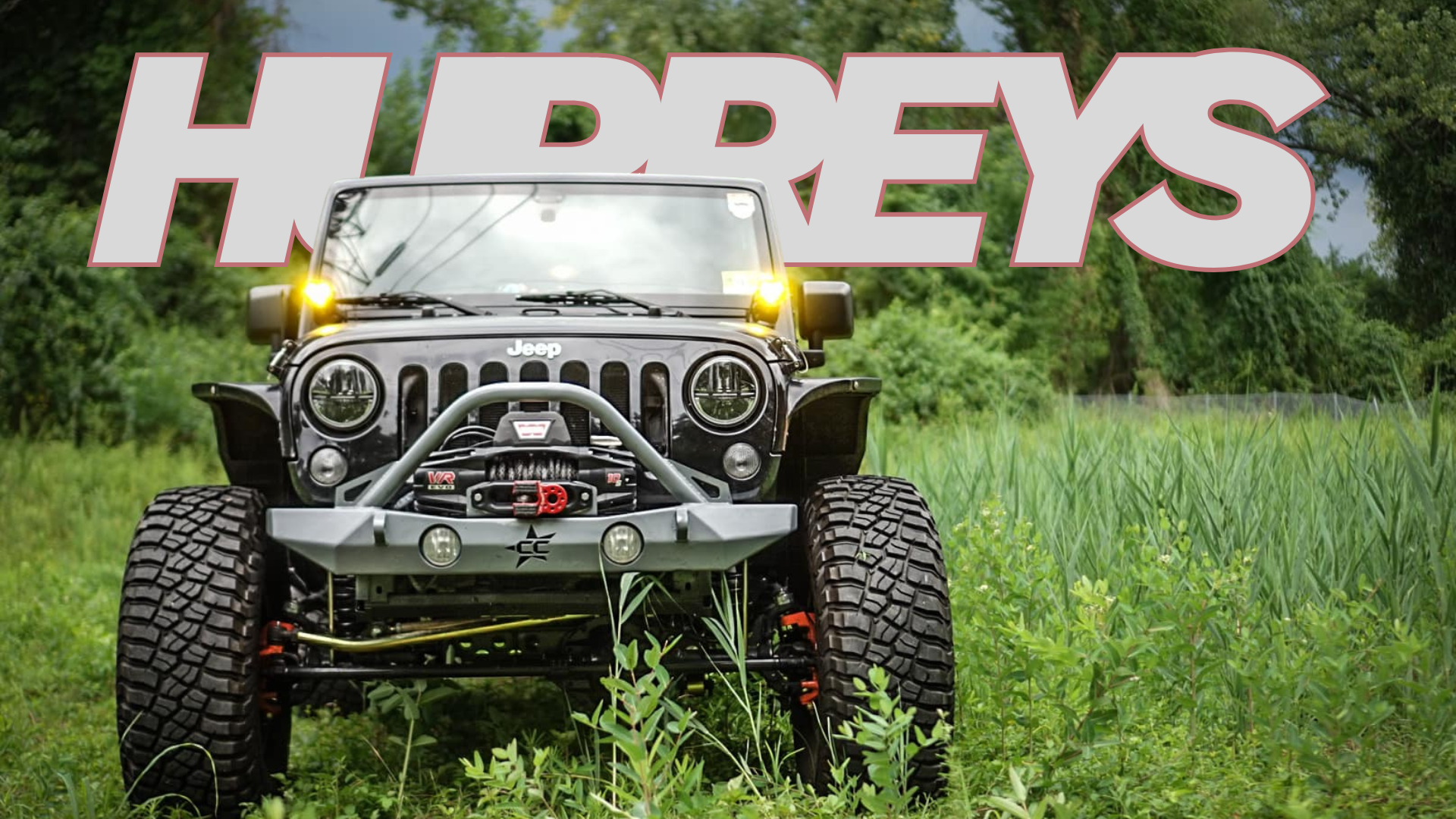Jeep in a grassy field with 'HURREYS' branding in the background